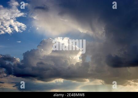 Blue sky just before the storm. Sun rays goes through the clouds. Some clouds are white, some not. A storm is coming. Stock Photo