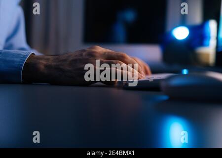 Close-up hands of unrecognizable man writing message to social network on wireless keyboard at night Stock Photo