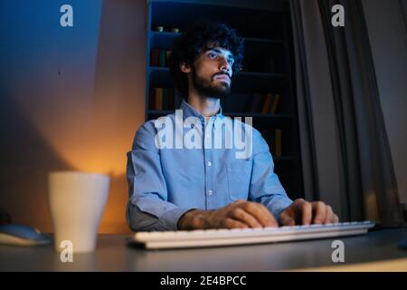 Thoughtful young businessman working on computer at late night at home office. Stock Photo
