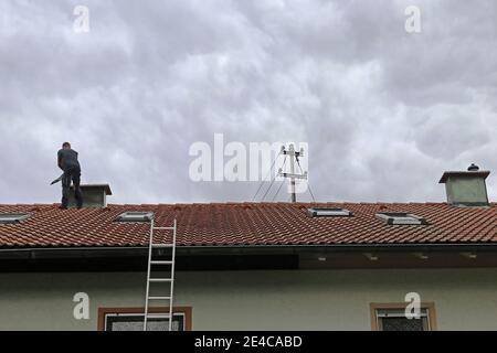 A chimney sweeper on the roof cleans a chimney with a brush Stock Photo