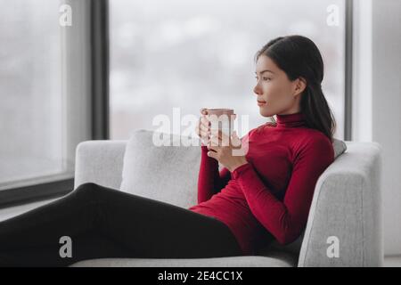 Happy Asian woman relaxing at home during coronavirus lockdown feeling calm and positive enjoying drinking coffee alone indoors. Mental health Stock Photo
