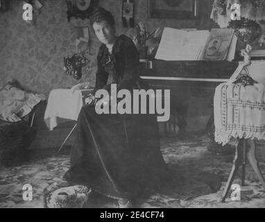 American archive monochrome portrait of a woman sitting in a living room with a piano and Victorian furniture. Taken in the late 19th century in Port Byron, NY, USA Stock Photo