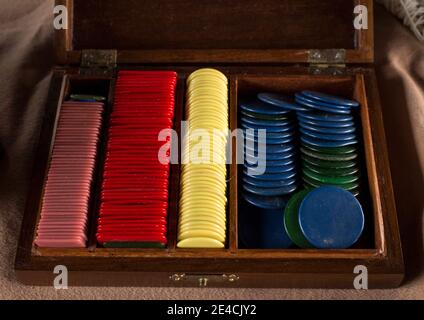 Multiples plastic poker chips (or used for another game) inside beautiful old crafted wooden box. Different colors of chips stacked all together Stock Photo