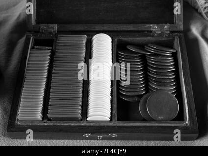 Multiples plastic poker chips (or used for another game) inside beautiful old crafted wooden box. Different colors of chips stacked all together Stock Photo