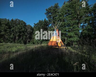 Tipi with fire on a meadow at night in the moonlight Stock Photo