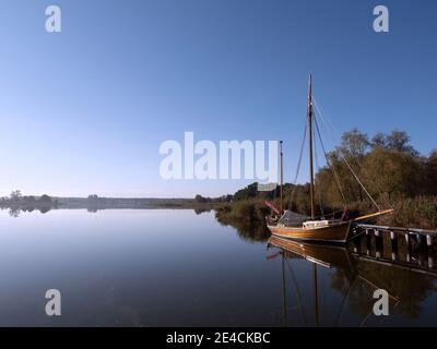 A Zeesboot on the shore is illuminated by the morning sun and is reflected in the water Stock Photo