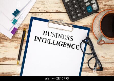 BUSINESS INTELLIGENCE is written in a document on the office desk with office accessories. Stock Photo