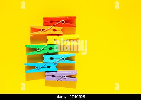 Mood-boosting color concept, multi-colored wooden multi-colored clothespins in a row on a yellow paper background. Creative minimalistic design, flat Stock Photo