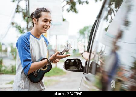 man busker playing on ukulele at city road during the day Stock Photo