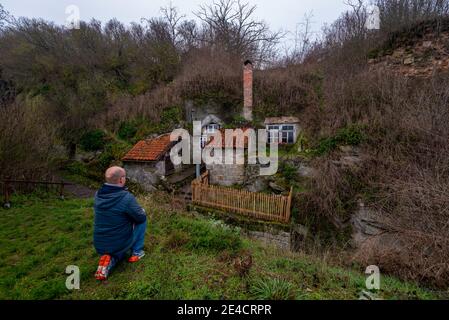 Germany, Saxony-Anhalt, Langenstein, man kneels in front of a cave dwelling, carved in sandstone from 1855 by farm workers' families, rock dwellings are reminiscent of the Shire from the bestsellers “The Lord of the Rings” and “The Hobbit” by the British writer JRR Tolkien. Stock Photo