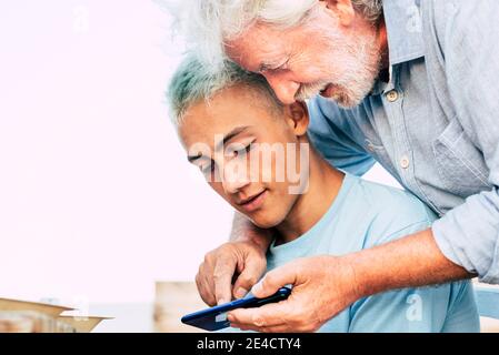 Portrait of young and old people grandfather and grandson together using a modern smart phone - family and friends concept with teenager and senior man enjoying technoogy together Stock Photo