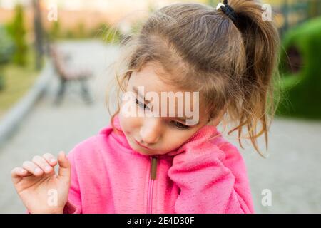 A little girl in a pink hoodie with a sad and tearful face is holding her ear. Ear pain, otitis media, swelling of the cheek, gums, toothache, childre Stock Photo