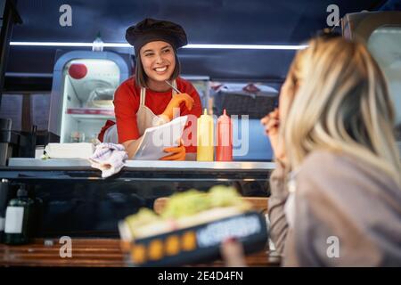 young female listening suggestions from a customer who is eating a sandwich in front of a fast food service