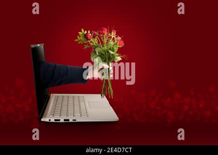 Hand of a man with a bouquet of roses coming out of a laptop screen, digital love on Valentines day with social distance during covid-19 pandemic, red Stock Photo