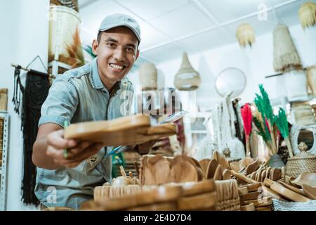 smiling man holds a craft item and looks at the camera while checking the item list among craft items in the crafting gallery Stock Photo