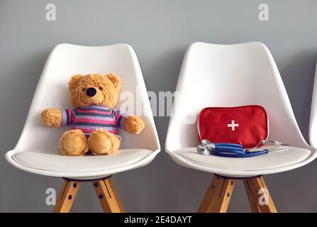 Teddy bear, first-aid kit and stethoscope on two chairs in pediatric clinic waiting room Stock Photo