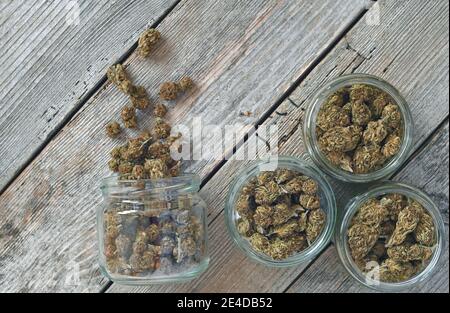 Dry and trimmed cannabis buds stored in a glas jars on a wooden table Stock Photo
