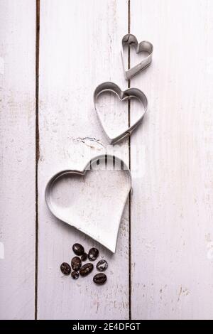 Composition of heart-shaped cookie molds with some coffee beans on a white wooden board. Let your love fligh. Stock Photo