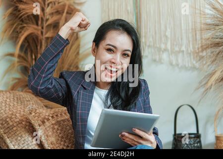 a happy beautiful woman in a blazer with hands up uses a digital tablet with a background in many crafts Stock Photo