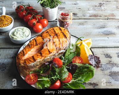 grilled fish steak salmon, trout with salad and tomatoes, white sauce, on plate Stock Photo