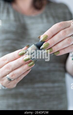 Woman's hand with long nails and light and dark green manicure with bottles of nail polish. Stock Photo