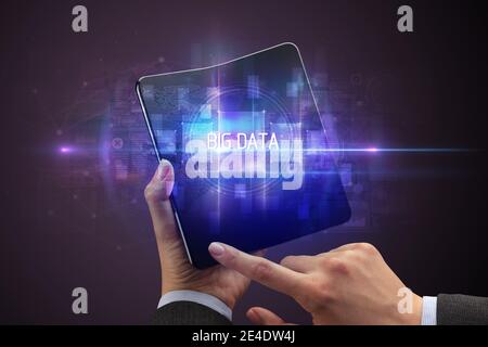 Businessman holding a foldable smartphone with BIG DATA inscription, new technology concept Stock Photo
