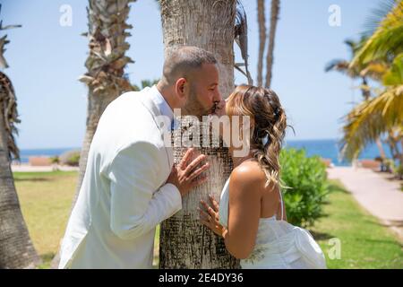 Groom and bride kissing in a park, newlyweds couple during an amazing sunny day celebrate their wedding kissing. Stock Photo
