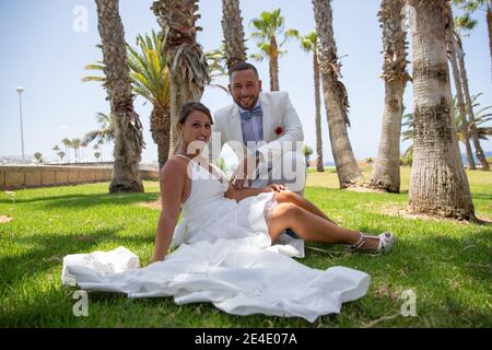Italian Newly married couple is happy after getting married. Bride sitting on a grass field next to the groom. Stock Photo