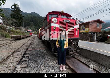 Beatiful tourist pose with red train on Alishan Forest Railway stop on the platform of Zhaoping railway station in Alishan, Taiwan. Stock Photo