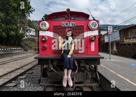 Beatiful tourist pose with red train on Alishan Forest Railway stop on the platform of Zhaoping railway station in Alishan, Taiwan. Stock Photo