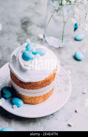 Easter cake kulich. Traditional Easter sweet bread decorated meringue and blue candy cane shape eggs on plate on gray stone table background. Copy spa Stock Photo