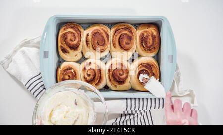 Flat lay. Glazing freshly baked cinnamon rolls in a blue baking pan. Stock Photo