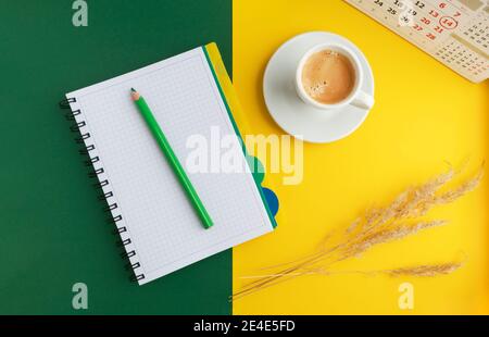 Open book, notebook, pencil, cup of coffee and dried flowers on a bright yellow-green background. Stock Photo