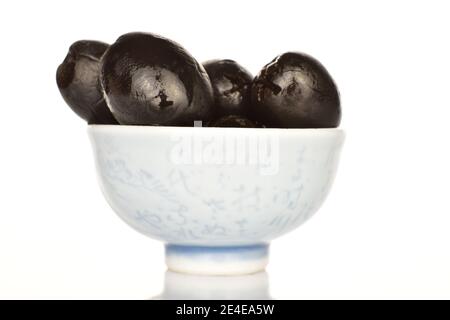 Several whole rounded black canned spicy aromatic olives, lie in a ceramic plate, on a white background. Stock Photo