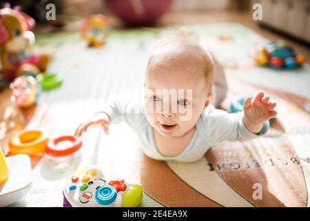 Wonderful baby girl laying on colourful mat at home. Adorable cute joyful toddler playing in kids room, smiling, childhood and childcare concept Stock Photo