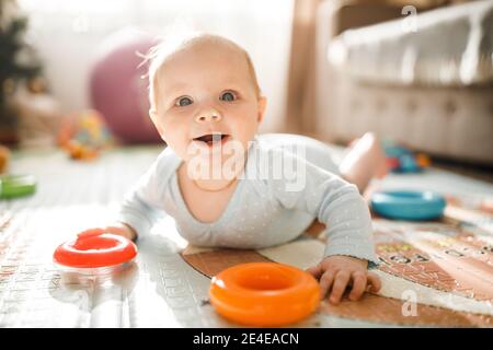 Wonderful baby girl laying on colourful mat at home. Adorable cute joyful toddler playing in kids room, smiling, childhood and childcare concept Stock Photo