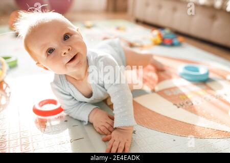 Wonderful baby girl laying on colourful mat at home. Adorable cute joyful toddler playing in kids room, smiling, childhood and childcare concept Stock Photo