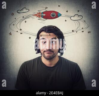 Silly young man makes funny dumb faces with crossed eyes. Body language emotional reaction. Dizzy daydreaming, stars and rocket making circles around Stock Photo