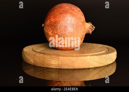 One whole dark red ripe juicy sweet pomegranate, on a wooden brown round stand, on a black background. Stock Photo