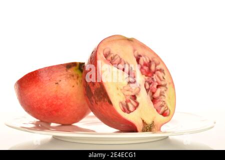 Two halves of organic ripe pomegranates on a ceramic plate, close-up, isolated on a white background. Stock Photo