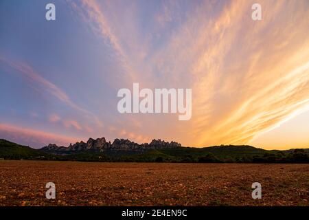 Sunset on the mountain of Montserrat, the most famous mountain in Catalonia. Clouds in the sky completely orange. Stock Photo