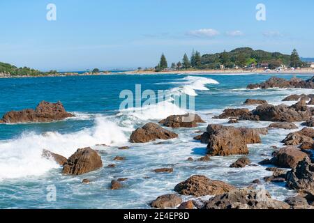Rocky foreshore at base of Mount Maunganui with waves surging in. and Main Beach in background. Stock Photo