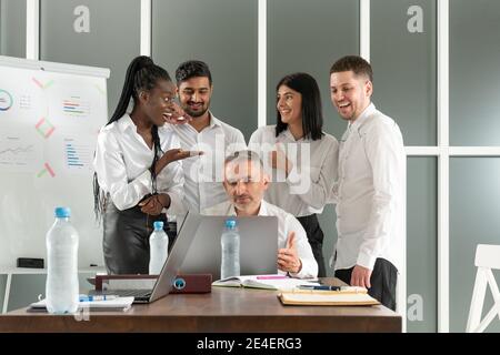 Male team leader listening to diverse colleagues questions, sitting together at table in office. Mixed race young teammates discussing project details Stock Photo