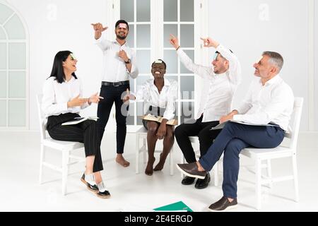 Pretty young multiethnic designer coworkers enjoying free time and raising togetherness and team spirit while sitting in a circle in the office and pl Stock Photo