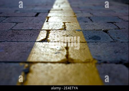 detail of a yellow line painted on cobblestones as a traffic marker Stock Photo