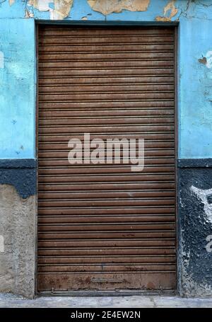 detail of a closed door with an old and rusted shutter on an old facade with a blue and deteriorated wall Stock Photo