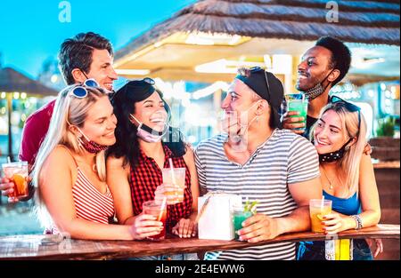 Young international friends talking at beach cocktail bar with open face mask - New normal tourism concept with millennial people having fun together Stock Photo