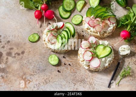 Sandwiches crispbread with ricotta, radish and fresh cucumber on a light or slate countertop. Copy space. Stock Photo