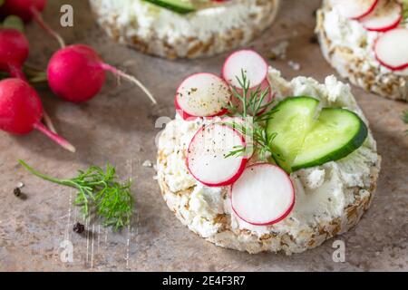 Sandwiches crispbread with ricotta, radish and fresh cucumber on a light or slate countertop. Stock Photo