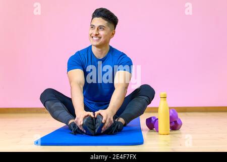 Young Hispanic man practicing yoga on his mat at gym on pink background. High quality photo Stock Photo